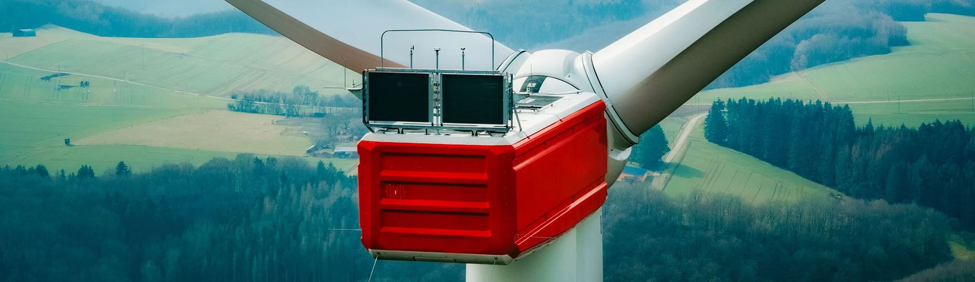 A red box positioned atop a wind turbine, contrasting against the blue sky and white turbine blades.
