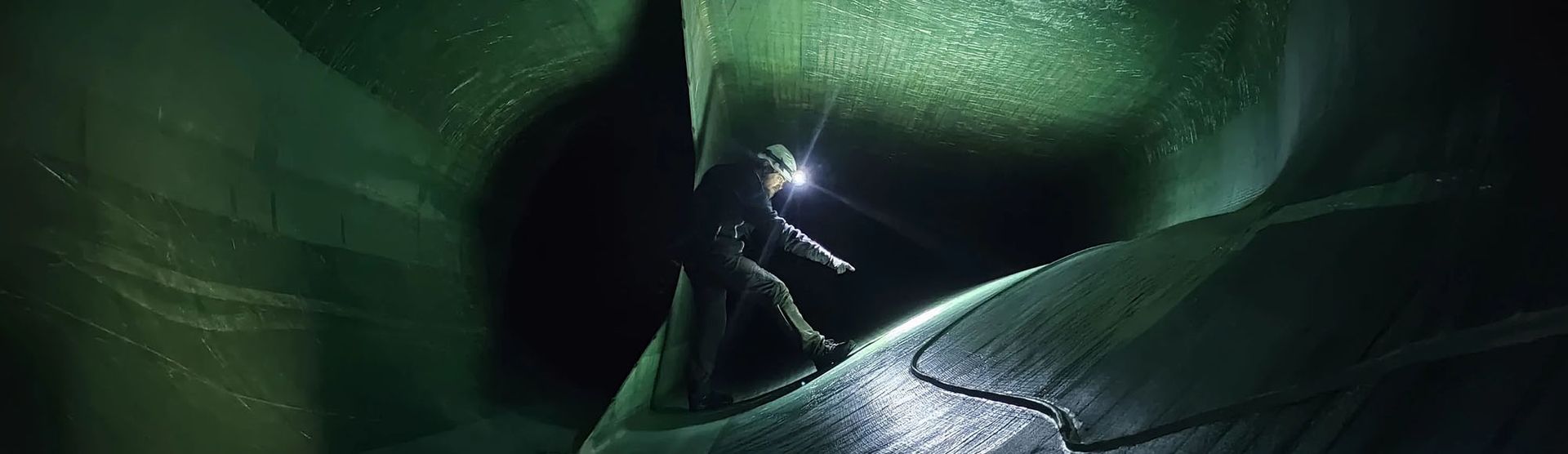 A man stands confidently in the center of a lush green tunnel, surrounded by vibrant foliage and natural light.